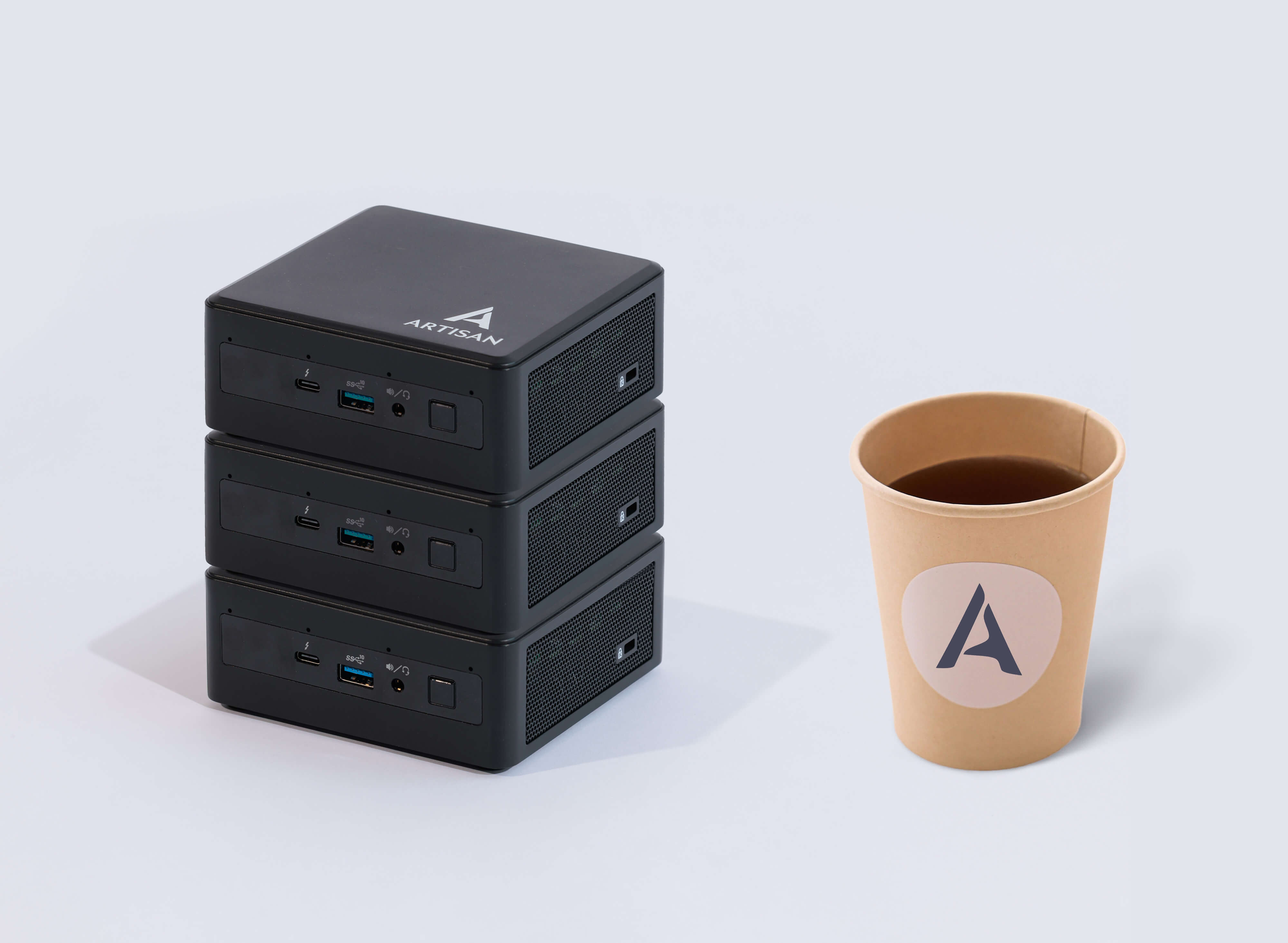 Stack of three compact Artisan edge devices beside a branded coffee cup for size comparison.